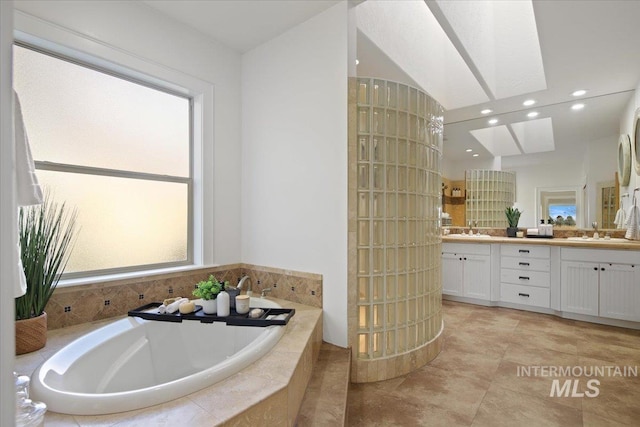 bathroom featuring a relaxing tiled tub, vanity, and a skylight