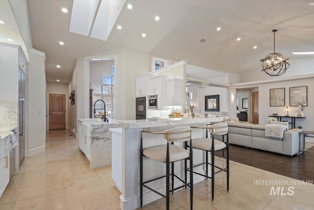 kitchen with pendant lighting, a breakfast bar, white cabinetry, an inviting chandelier, and high vaulted ceiling