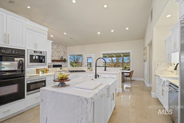 kitchen with black appliances, an island with sink, a fireplace, light stone countertops, and white cabinets