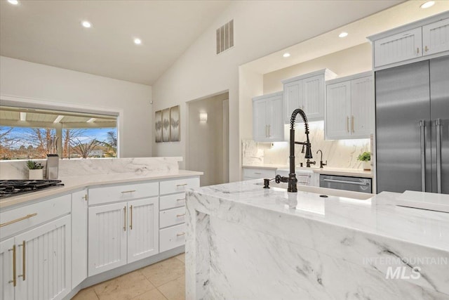 kitchen featuring vaulted ceiling, light tile patterned floors, stainless steel appliances, light stone countertops, and white cabinets