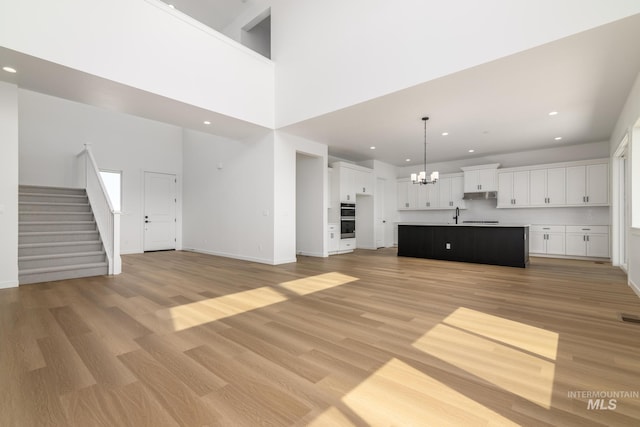 unfurnished living room featuring a notable chandelier, light wood-type flooring, and a high ceiling