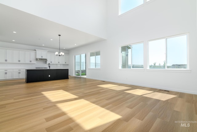 unfurnished living room featuring a notable chandelier, a healthy amount of sunlight, sink, and light hardwood / wood-style flooring