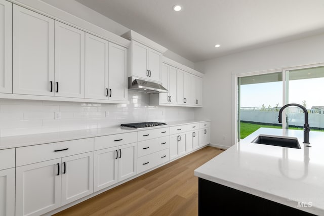 kitchen featuring sink, light hardwood / wood-style flooring, backsplash, stainless steel gas stovetop, and white cabinets