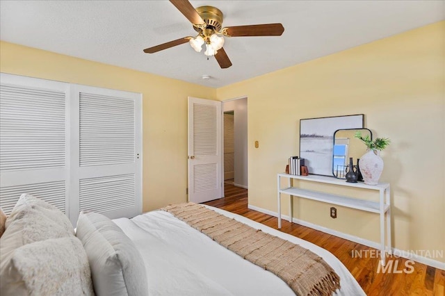 bedroom featuring a closet, baseboards, wood finished floors, and a ceiling fan