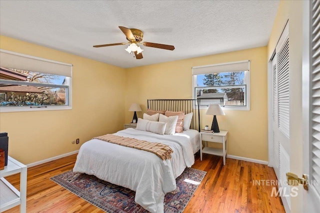 bedroom featuring multiple windows, a textured ceiling, baseboards, and wood finished floors