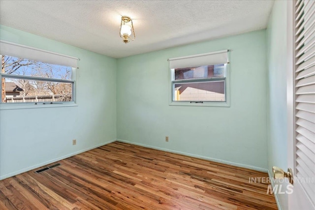 empty room featuring visible vents, baseboards, a textured ceiling, and wood finished floors