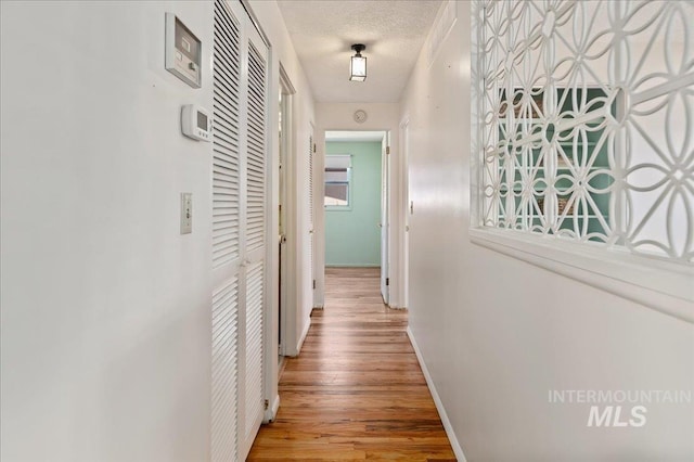 corridor featuring wood finished floors, baseboards, and a textured ceiling