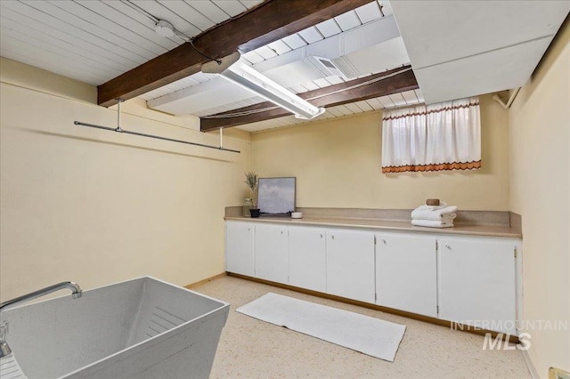 interior space with beamed ceiling, light speckled floor, light countertops, and white cabinetry