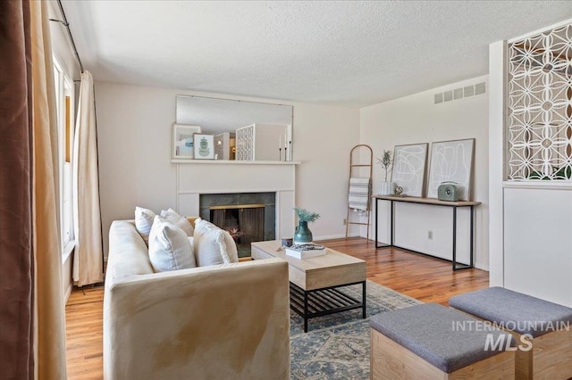 living room with visible vents, a fireplace, a textured ceiling, and wood finished floors