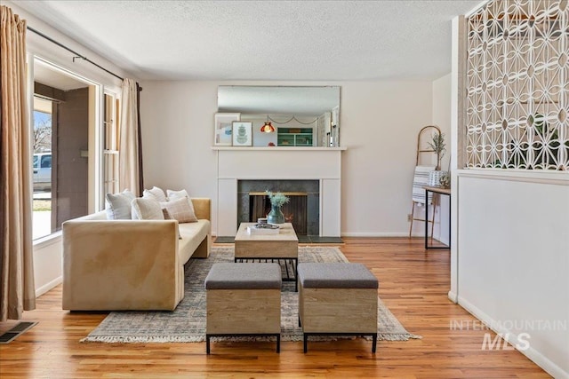 living area with wood finished floors, baseboards, visible vents, a fireplace, and a textured ceiling