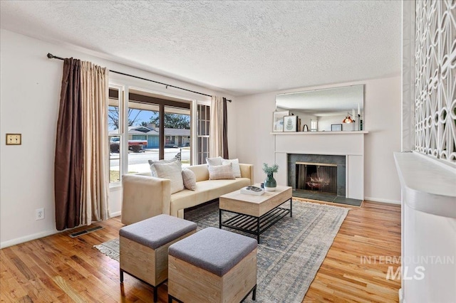 living area with wood finished floors, baseboards, visible vents, a tile fireplace, and a textured ceiling