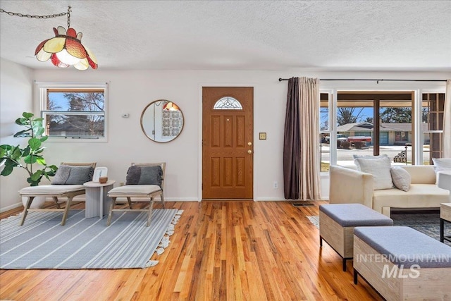 foyer with light wood-type flooring, baseboards, and a textured ceiling