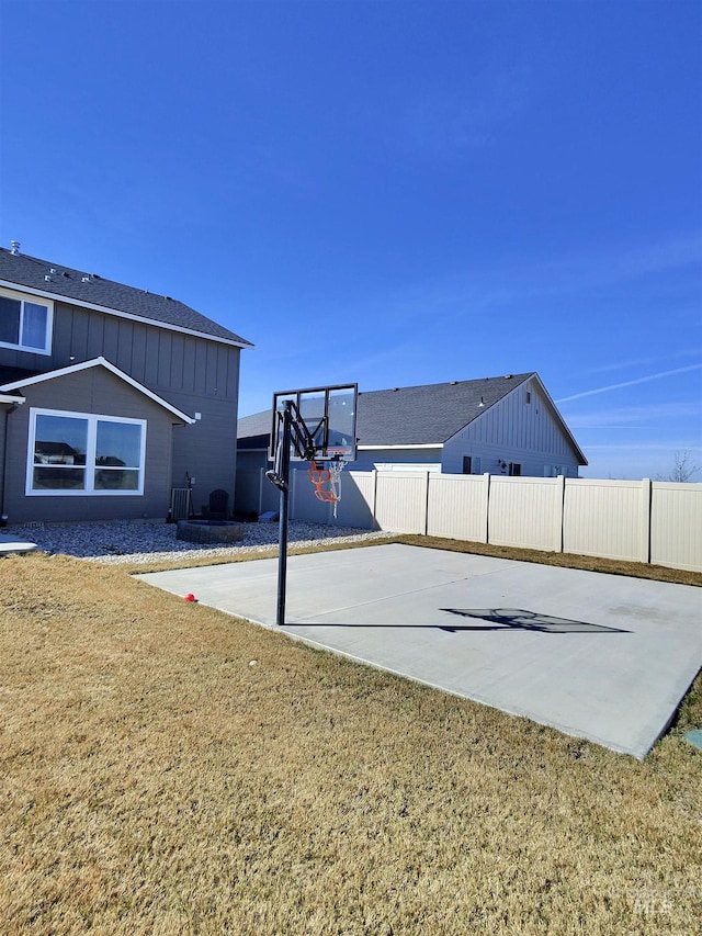 view of basketball court featuring a yard, fence, and basketball hoop
