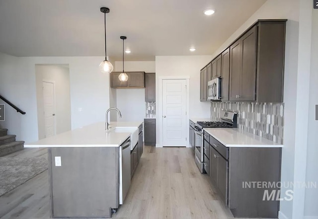 kitchen with light wood-style floors, light countertops, a sink, stainless steel appliances, and decorative backsplash