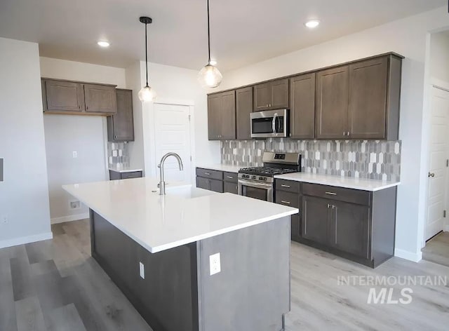 kitchen with a sink, tasteful backsplash, light wood-type flooring, and appliances with stainless steel finishes