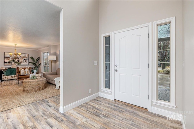 entrance foyer featuring a textured ceiling, light wood-type flooring, crown molding, and a notable chandelier