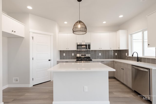 kitchen featuring appliances with stainless steel finishes, a sink, light wood finished floors, and tasteful backsplash