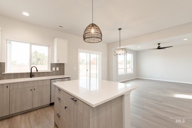 kitchen with light wood finished floors, decorative backsplash, dishwasher, light countertops, and a sink