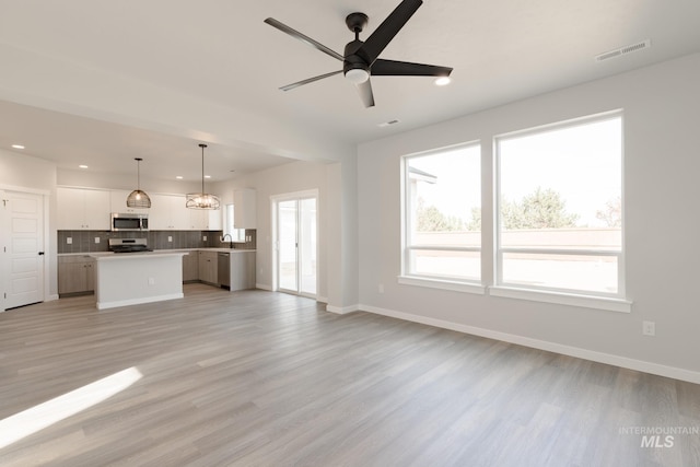 unfurnished living room with visible vents, light wood-style flooring, a sink, baseboards, and ceiling fan with notable chandelier