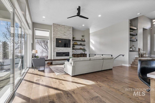 living room with hardwood / wood-style floors, a stone fireplace, recessed lighting, and a ceiling fan