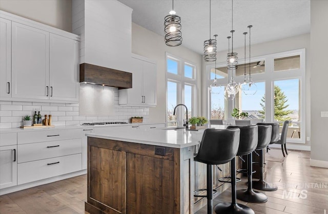 kitchen with a kitchen island with sink, backsplash, light wood-style flooring, and a sink