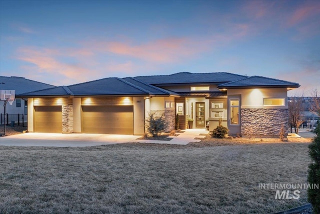 prairie-style house featuring stucco siding, stone siding, an attached garage, and a tiled roof