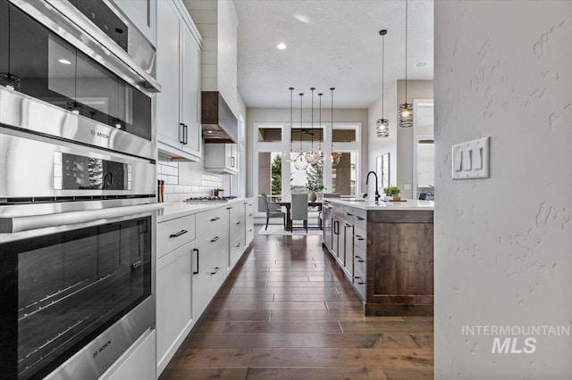 kitchen featuring decorative backsplash, appliances with stainless steel finishes, light countertops, and wall chimney range hood