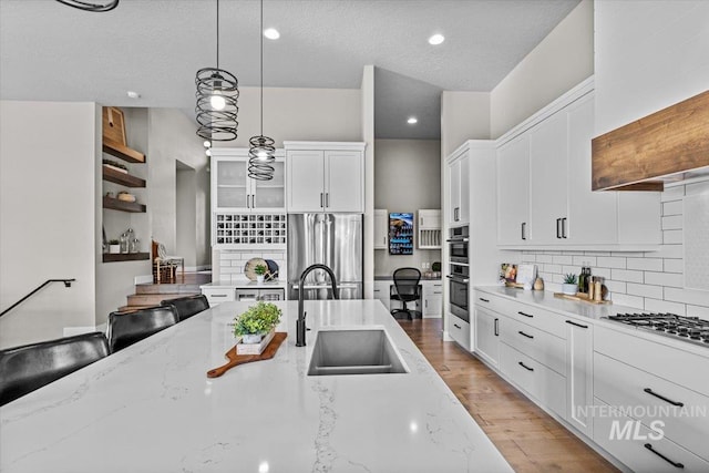 kitchen featuring light wood-style flooring, a sink, white cabinets, appliances with stainless steel finishes, and decorative light fixtures