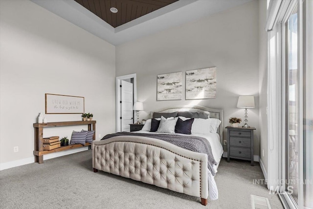 bedroom featuring baseboards, light carpet, a raised ceiling, and a towering ceiling