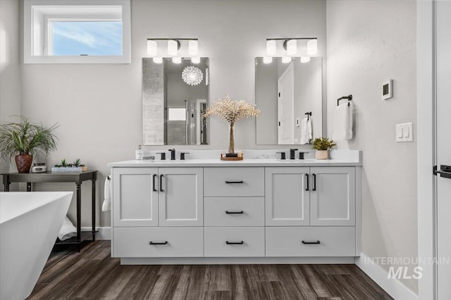 full bathroom with double vanity, a sink, baseboards, and wood finished floors