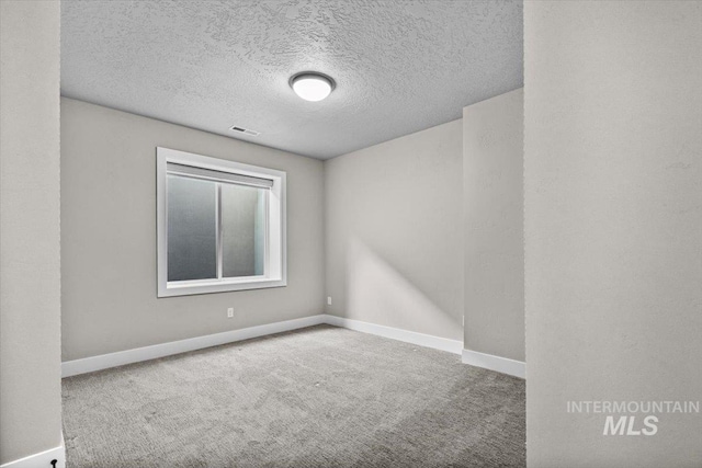 carpeted spare room featuring visible vents, baseboards, and a textured ceiling