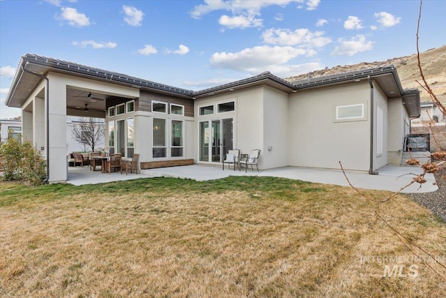 rear view of house featuring a patio, stucco siding, a lawn, and ceiling fan