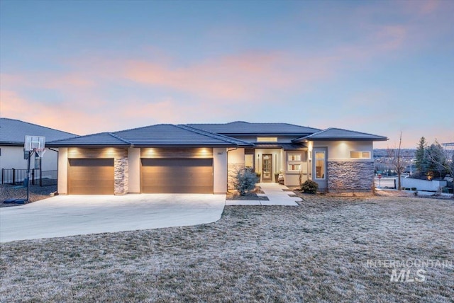 prairie-style home with fence, an attached garage, concrete driveway, stone siding, and a tile roof