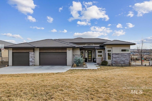 prairie-style house featuring a front lawn, an attached garage, stone siding, and concrete driveway