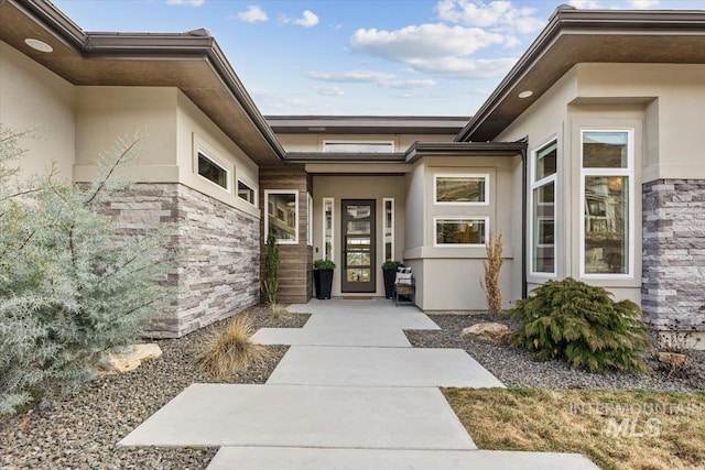 view of exterior entry featuring stone siding and stucco siding