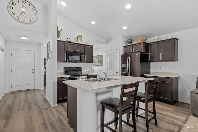 kitchen with a kitchen island with sink, light countertops, dark brown cabinets, and black appliances