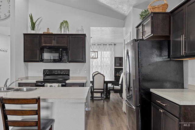 kitchen with light wood-style flooring, dark brown cabinetry, a sink, light countertops, and black appliances