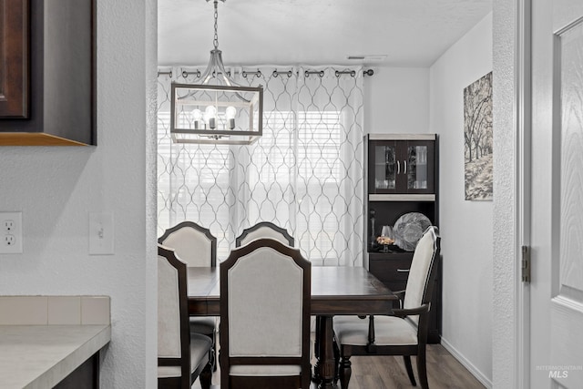 dining area featuring a textured wall, wood finished floors, visible vents, and baseboards