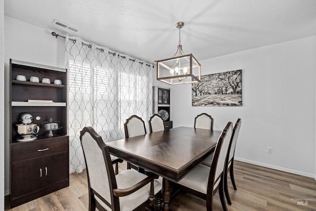 dining space with a chandelier, visible vents, baseboards, and wood finished floors