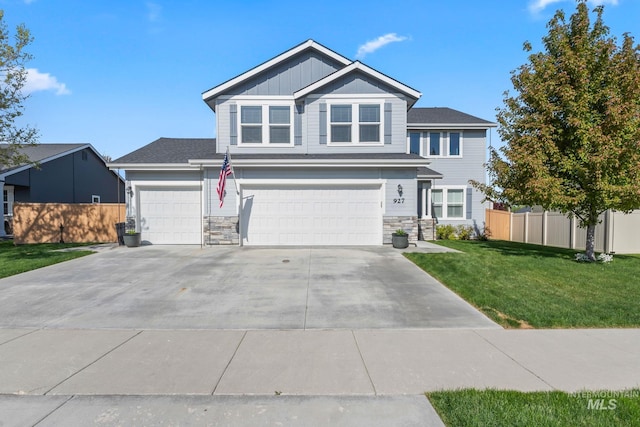 traditional-style house with a front yard, a garage, fence, concrete driveway, and stone siding