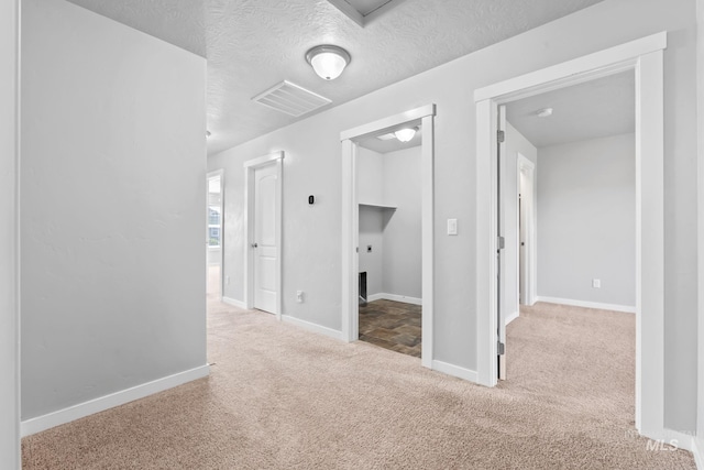 corridor featuring baseboards, carpet flooring, a textured ceiling, and visible vents