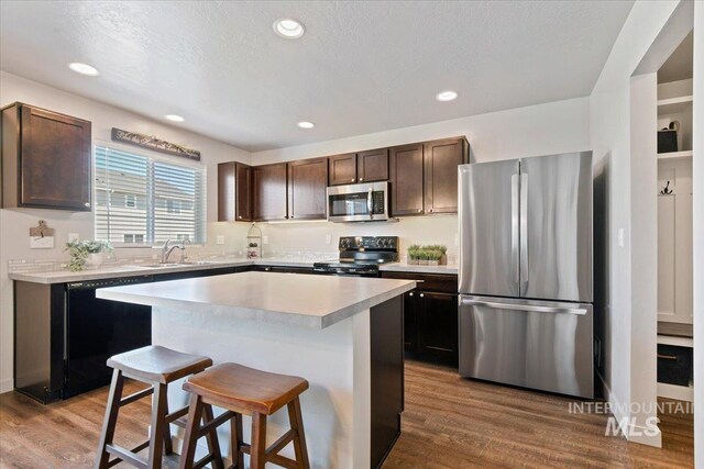 kitchen with black appliances, a sink, light countertops, a breakfast bar area, and dark brown cabinets