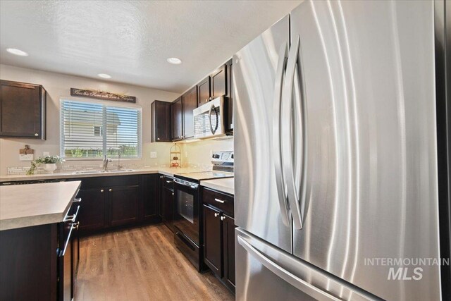 kitchen featuring stainless steel appliances, a sink, light wood finished floors, light countertops, and recessed lighting