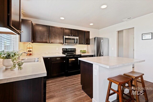 kitchen featuring stainless steel appliances, a sink, a kitchen breakfast bar, dark wood-type flooring, and light countertops