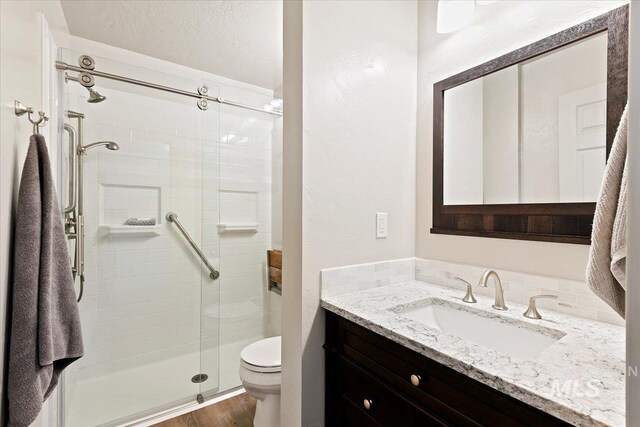 full bath with toilet, a stall shower, vanity, wood finished floors, and a textured wall