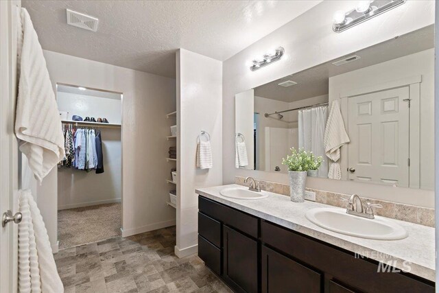 bathroom featuring a walk in closet, double vanity, baseboards, a shower with curtain, and a textured ceiling