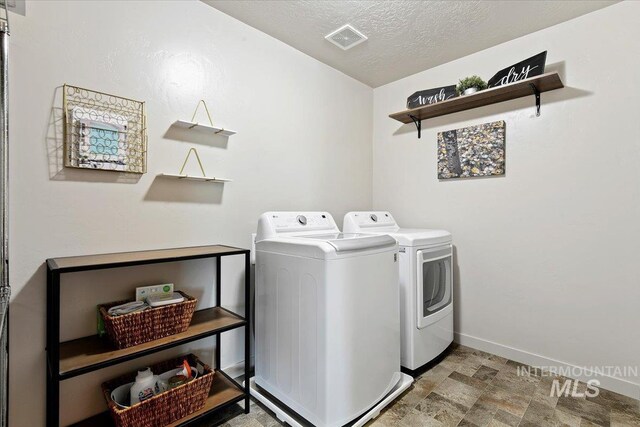 clothes washing area featuring independent washer and dryer, baseboards, stone finish floors, and a textured ceiling
