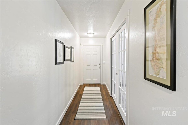 corridor with dark wood-style flooring, baseboards, and a textured ceiling