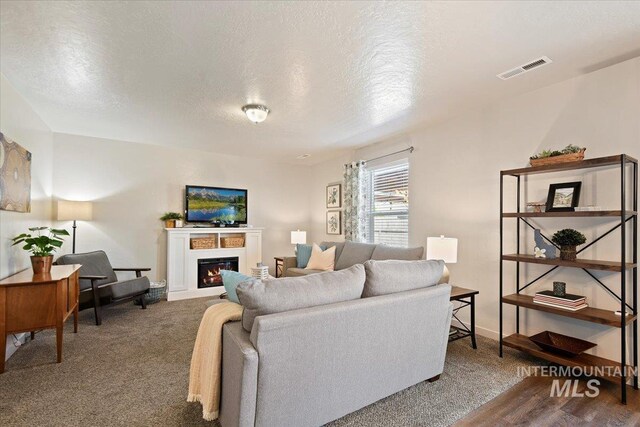 carpeted living room with a textured ceiling, a lit fireplace, and baseboards
