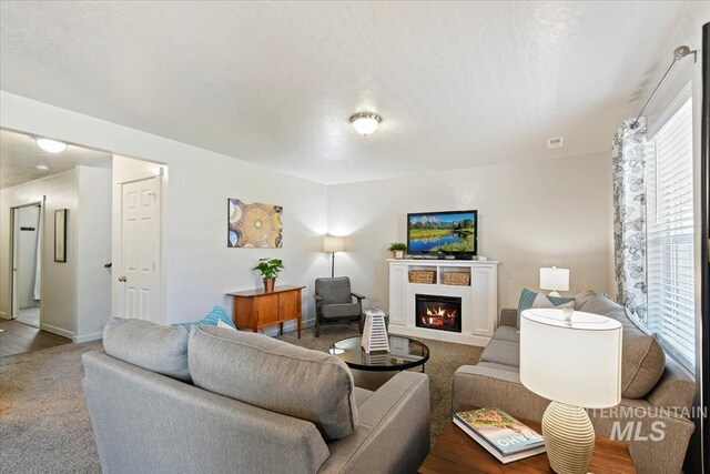 carpeted living room featuring a glass covered fireplace and baseboards